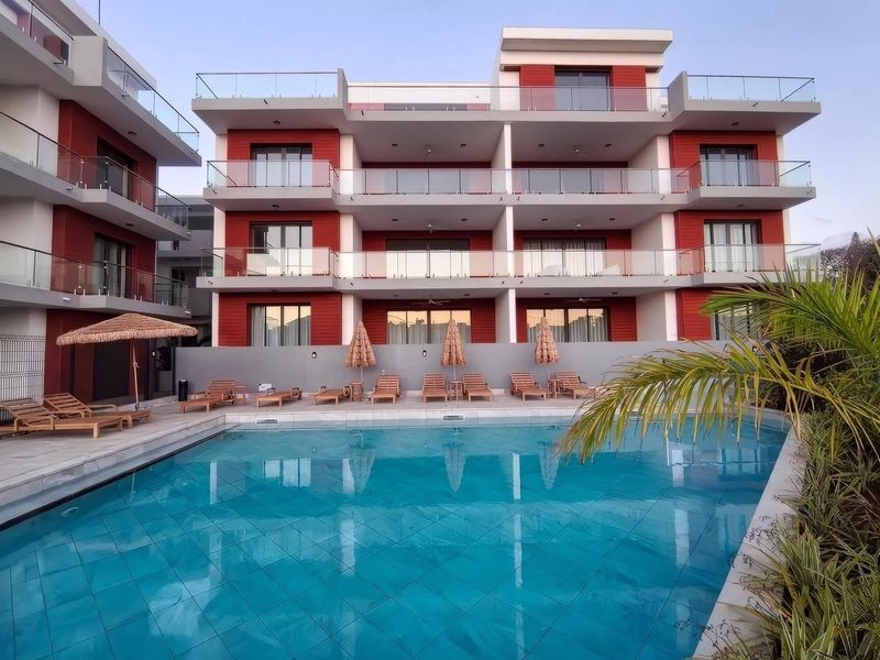 A modern apartment complex featuring a well-maintained swimming pool, tiled deck area, and multi-level balconies with glass balustrades.