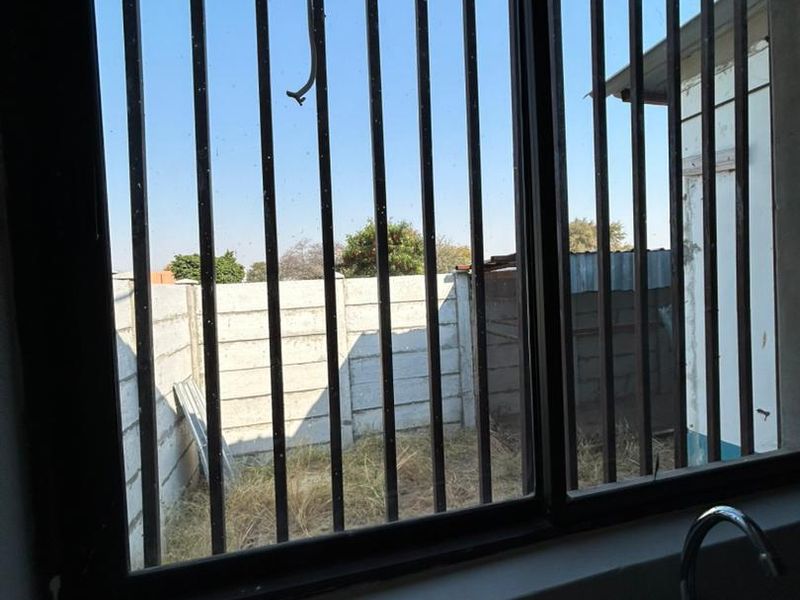 A view from a kitchen window featuring metal security bars, a sink, and a view of the rear yard with a concrete boundary wall.