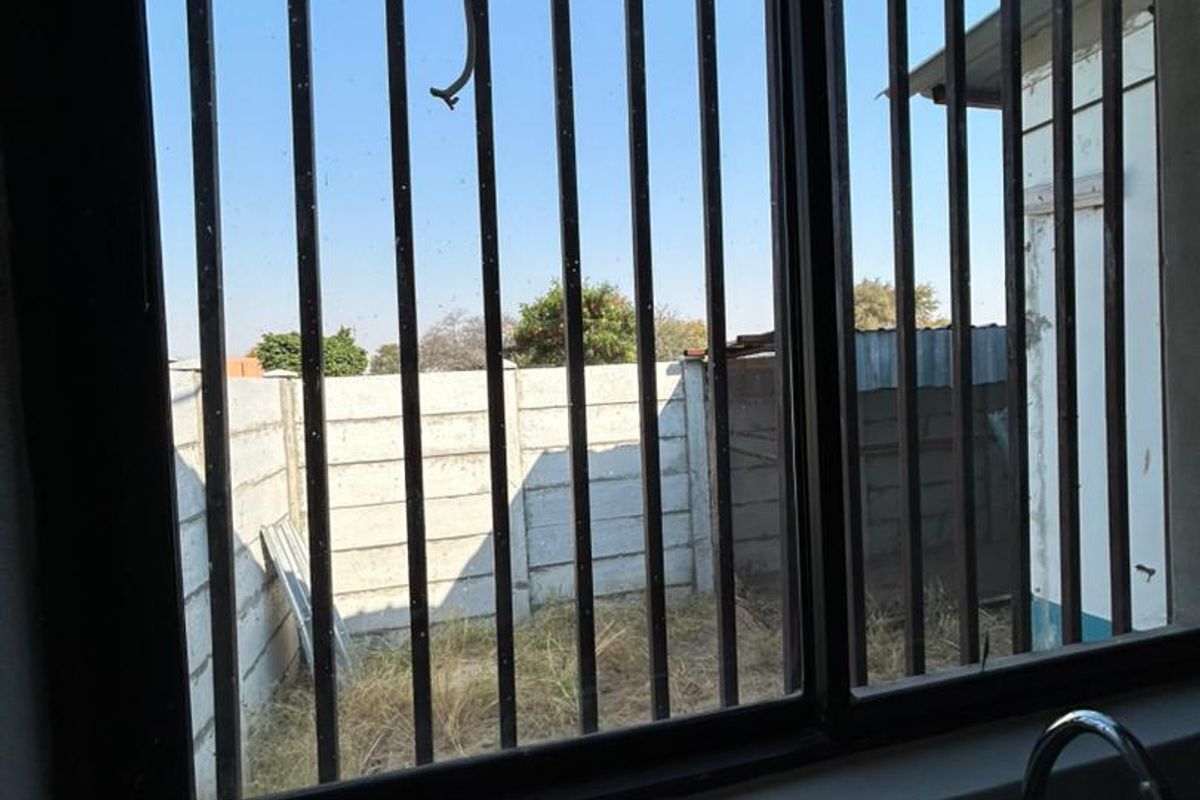 A view from a kitchen window featuring metal security bars, a sink, and a view of the rear yard with a concrete boundary wall.