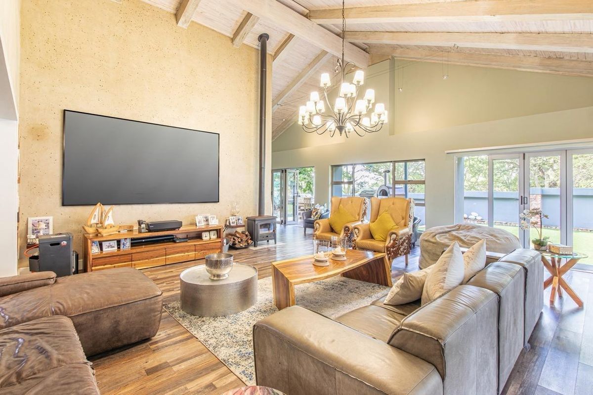 Spacious living room featuring a vaulted ceiling with exposed timber beams, a freestanding wood-burning fireplace, and large sliding glass doors opening to the garden.