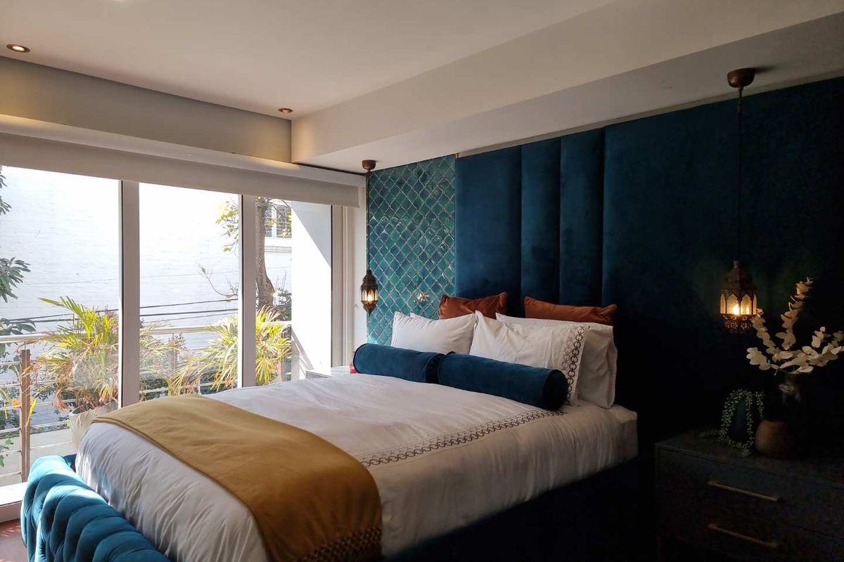 A well-appointed bedroom featuring a large window with natural light, recessed ceiling lighting, and a decorative feature wall behind the bed.