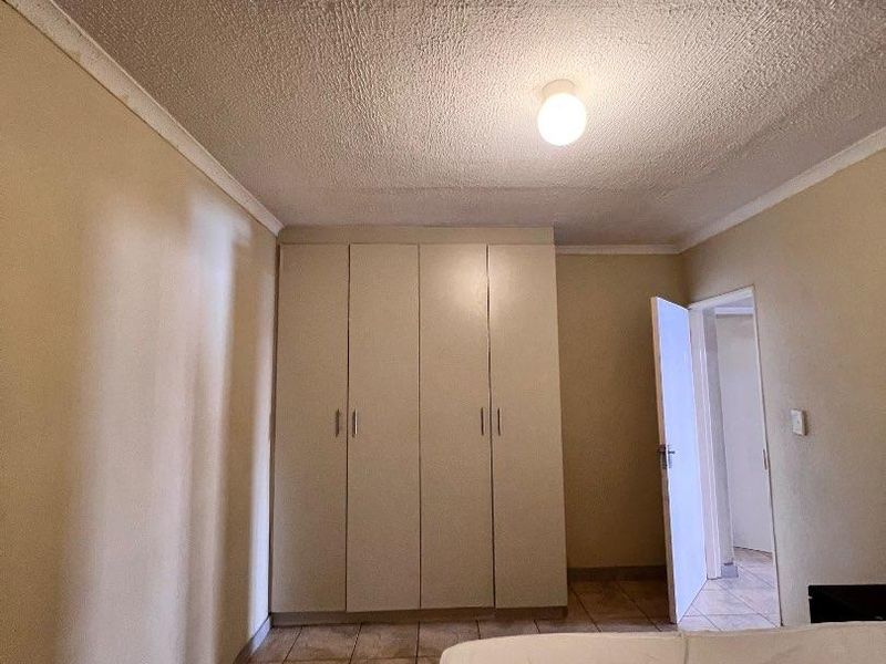 A bedroom featuring built-in cupboards, tiled flooring, and a textured ceiling, offering a functional space ready for cosmetic updates.