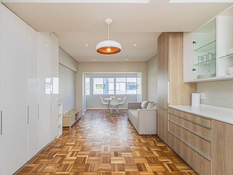 Modern open-plan living area featuring high-quality parquet flooring, extensive built-in cabinetry, and a bright, functional layout with integrated kitchen storage.