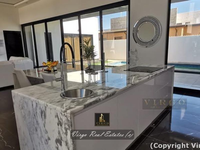 Modern open-plan living area featuring a marble kitchen island with integrated hob and sink, flowing seamlessly to the outdoor pool area through sliding doors.