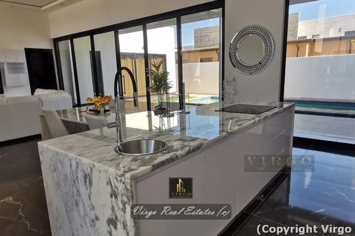 Modern open-plan living area featuring a marble kitchen island with integrated hob and sink, flowing seamlessly to the outdoor pool area through sliding doors.