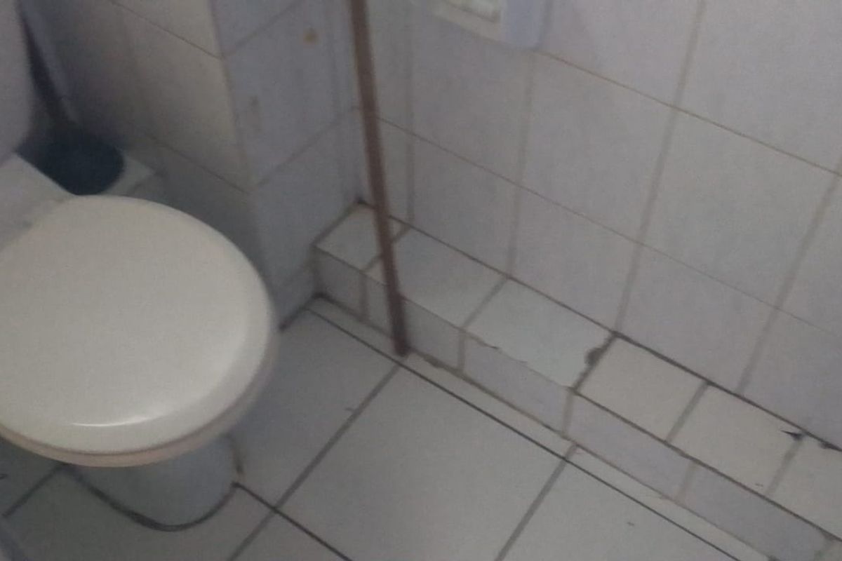 A small bathroom featuring a standard toilet with white ceramic wall and floor tiling showing signs of wear and damage.