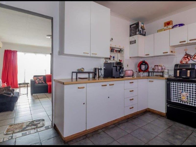 A functional kitchen featuring white cabinetry, laminate countertops, and tiled flooring, with an open-plan layout connecting to the adjacent living area.