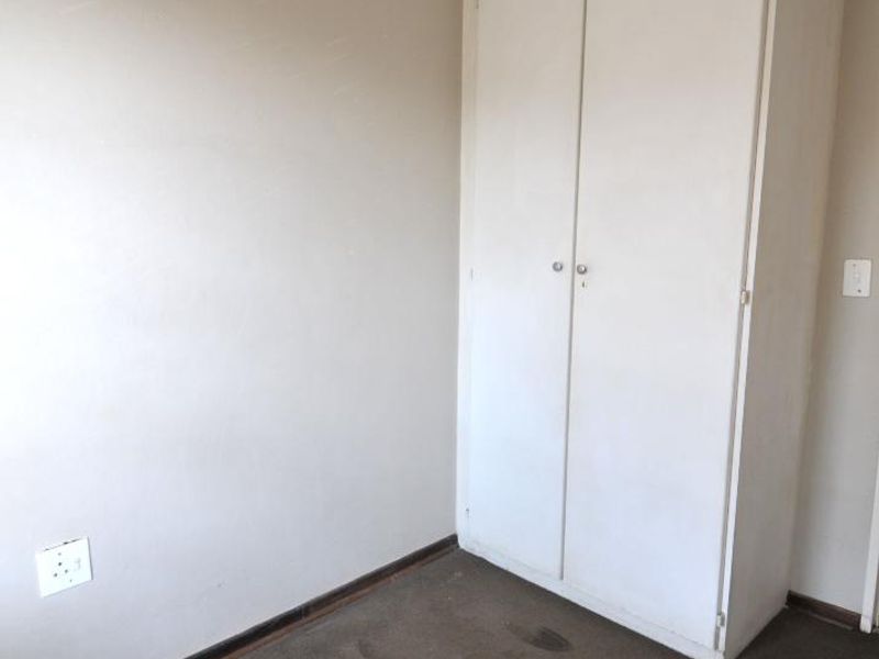 An empty bedroom featuring a built-in wardrobe, neutral wall finishes, and carpet flooring, offering a blank canvas for potential updates.