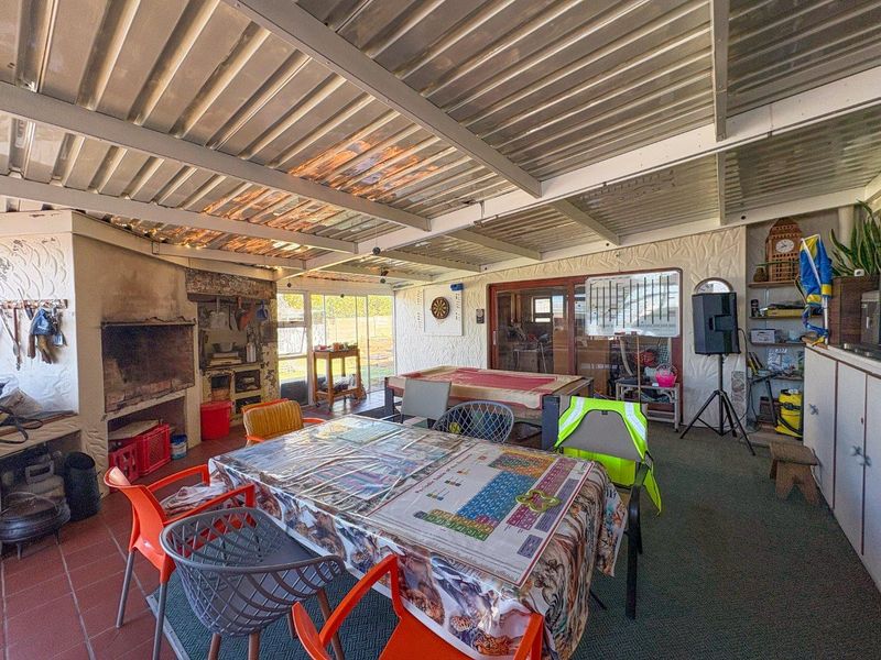 Covered outdoor patio area featuring a built-in braai, corrugated metal roofing, and direct access to the home through sliding glass doors.
