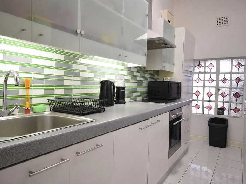 A well-maintained kitchen featuring modern white cabinetry, a stainless steel sink, built-in oven with hob, and a decorative tiled splashback.
