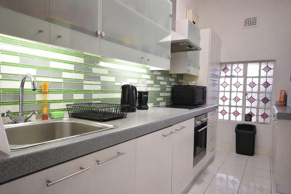 A well-maintained kitchen featuring modern white cabinetry, a stainless steel sink, built-in oven with hob, and a decorative tiled splashback.
