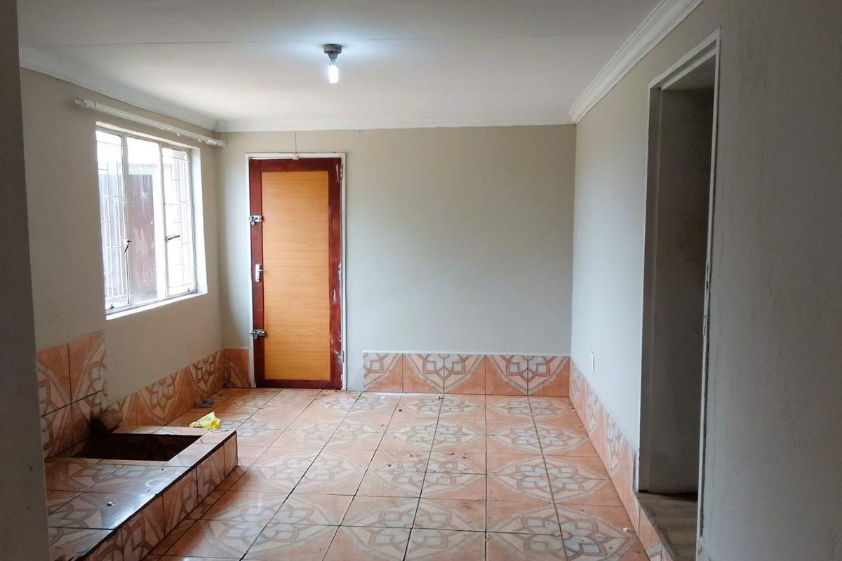 An empty utility or kitchen space featuring tiled flooring with a decorative pattern, a single door, and a window with security bars.