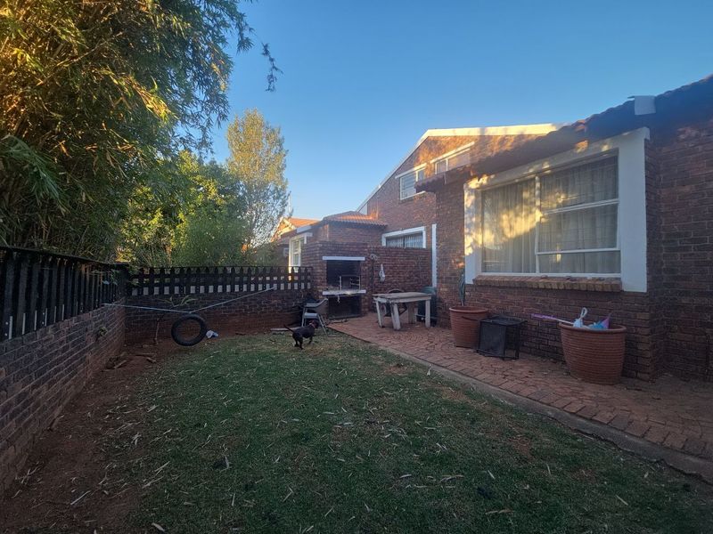 Rear garden area featuring a brick facade, paved patio space, and a built-in braai, offering potential for outdoor entertainment.