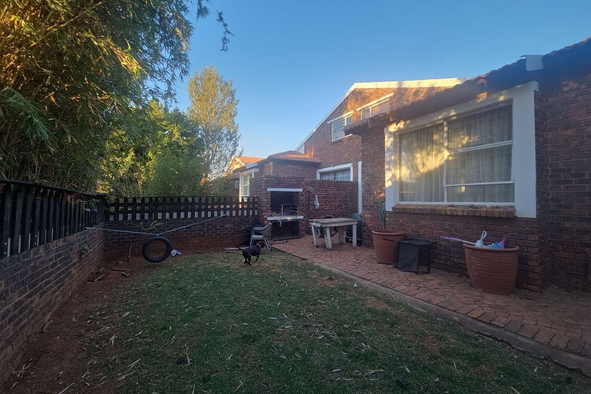Rear garden area featuring a brick facade, paved patio space, and a built-in braai, offering potential for outdoor entertainment.