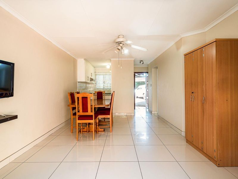 Open-plan living and dining area featuring neutral tiled flooring, coved cornicing, and a central ceiling fan, leading towards the kitchen and entrance.