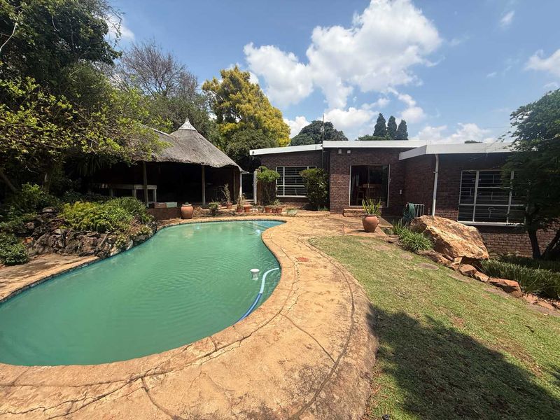 Outdoor pool area featuring a swimming pool, paved surround, and a traditional thatched lapa set against a brick house exterior.
