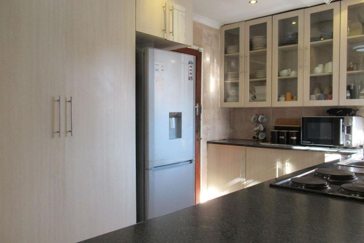 A functional kitchen featuring light-toned cabinetry, dark countertops, glass-fronted display cabinets, and a built-in electric hob.