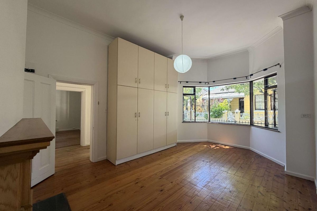 Spacious bedroom featuring polished timber flooring, a large built-in wardrobe, and a bright bay window overlooking the front garden.