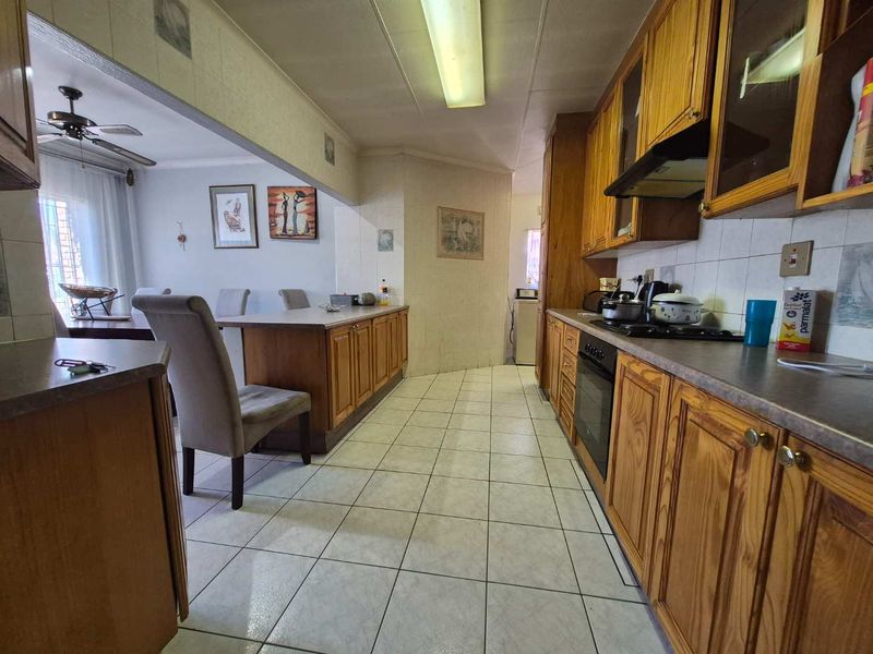 Open-plan kitchen and dining area featuring traditional wooden cabinetry, tiled flooring, and integrated cooking appliances, offering a functional layout with potential for modernization.