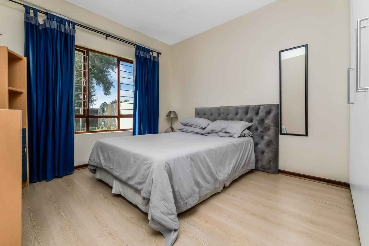 A bedroom featuring light-toned laminate flooring, a large window with blue curtains, and built-in cupboard storage.