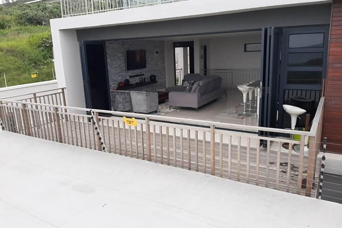 Spacious balcony featuring timber decking and electric fencing, seamlessly connecting to an open-plan living area through large folding glass doors.