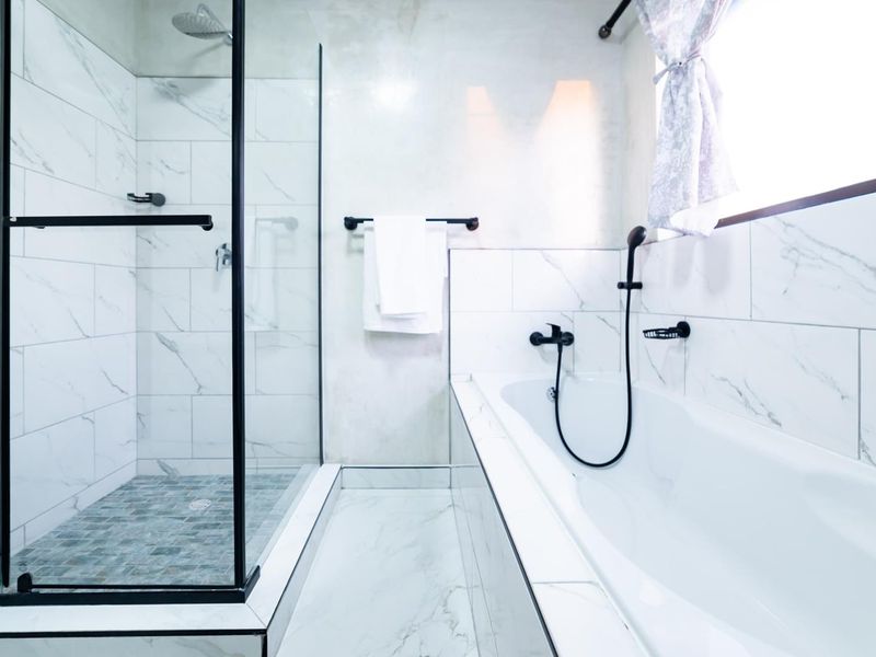 Modern bathroom featuring a walk-in shower with black-framed glass, a built-in bathtub, and elegant marble-look wall tiles with contemporary black matte fixtures.