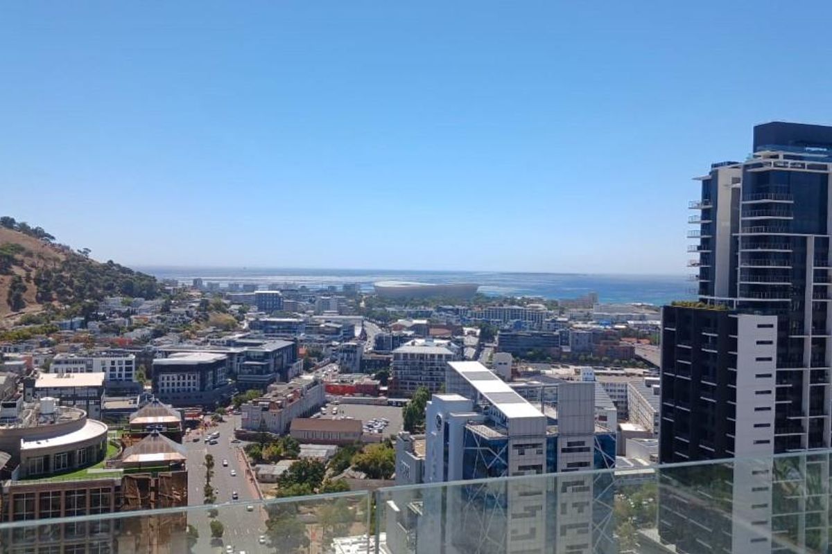 Elevated panoramic city and coastal view captured from a high-rise balcony with a modern glass balustrade.