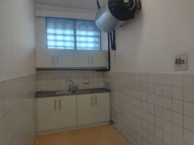 A functional laundry area featuring built-in cabinetry, a stainless steel sink, tiled splashbacks, and a wall-mounted electric water heater.
