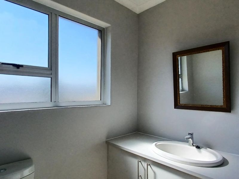 A clean and functional bathroom featuring a vanity cabinet with a drop-in sink, a toilet, and an aluminium-framed window with frosted glass.