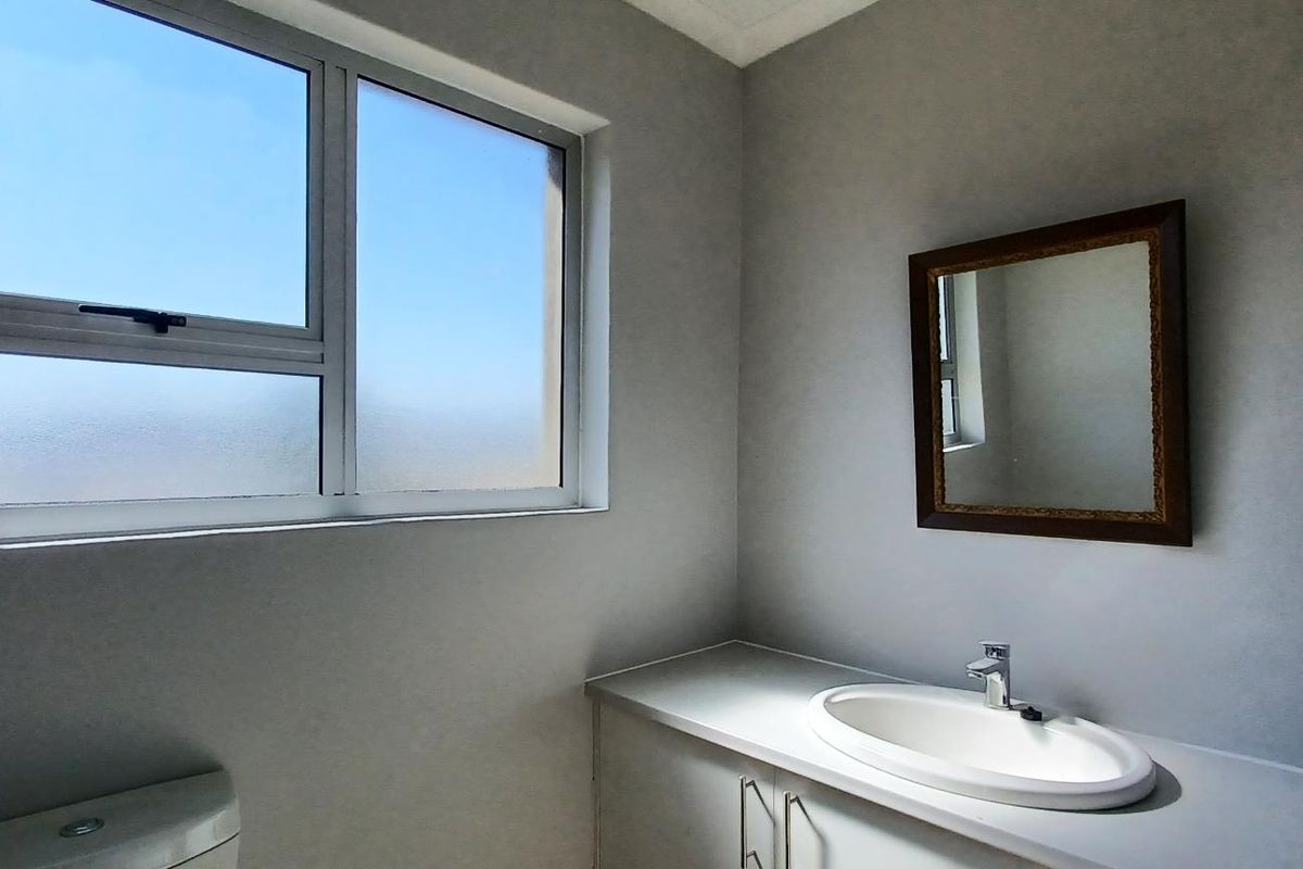 A clean and functional bathroom featuring a vanity cabinet with a drop-in sink, a toilet, and an aluminium-framed window with frosted glass.