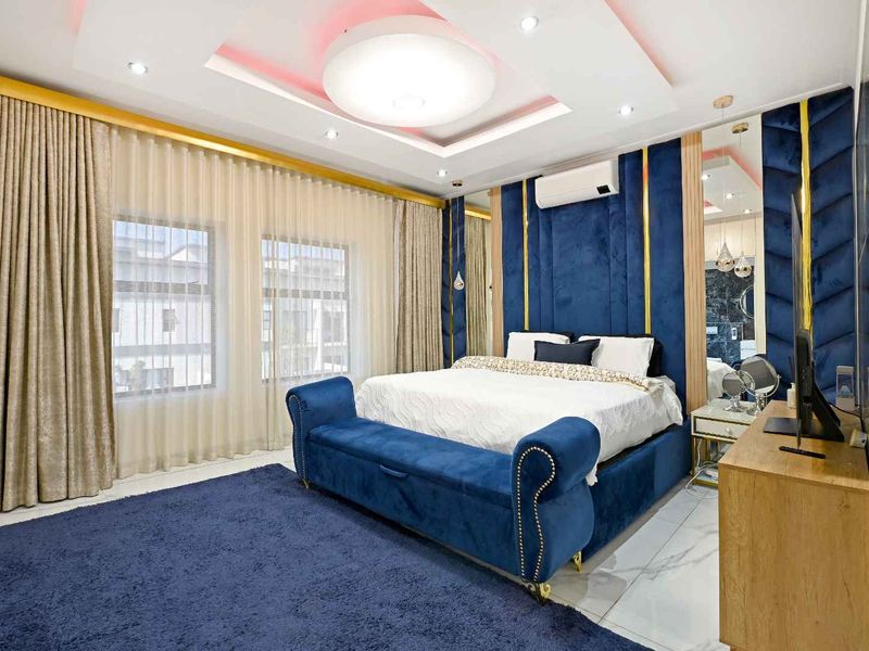 A modern, well-appointed bedroom featuring a recessed ceiling with ambient lighting, tiled floors, and integrated mirrored wall panels.