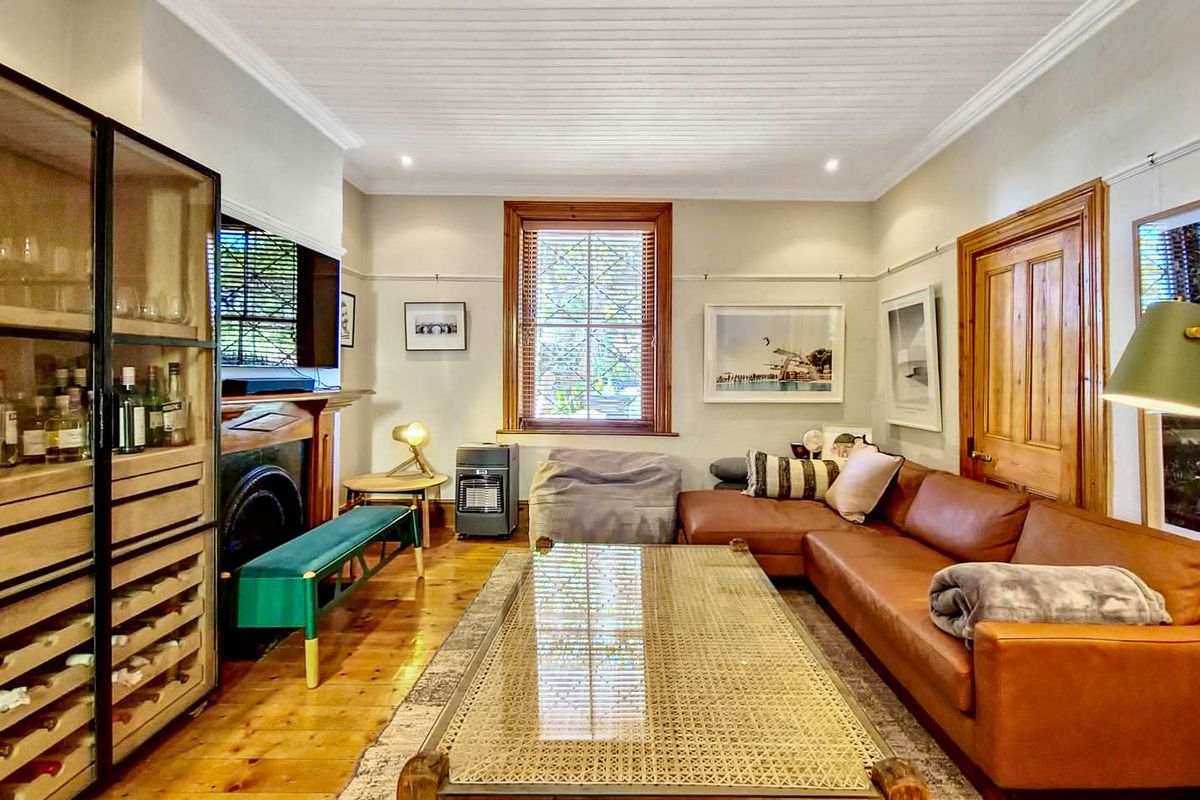 A cozy living room featuring polished timber flooring, a traditional fireplace with a mantelpiece, and classic timber door and window frames.