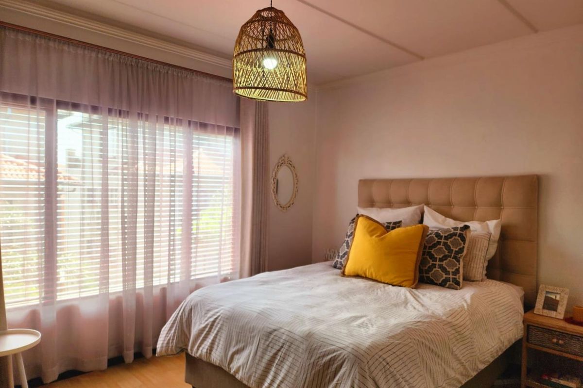 A well-lit bedroom featuring light wood-look flooring, large window with fitted blinds, and a neutral color palette.