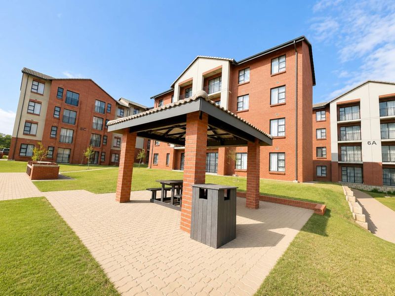 A well-maintained apartment complex courtyard featuring a brick gazebo, paved walkways, and landscaped green spaces between multi-story residential buildings.
