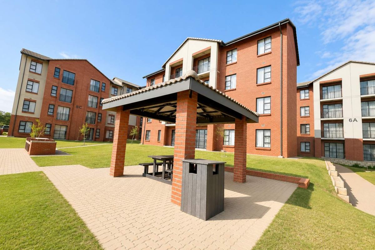 A well-maintained apartment complex courtyard featuring a brick gazebo, paved walkways, and landscaped green spaces between multi-story residential buildings.