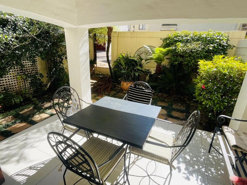A covered patio area featuring tiled flooring and a structural pillar, overlooking a private garden space with established greenery and boundary walls.