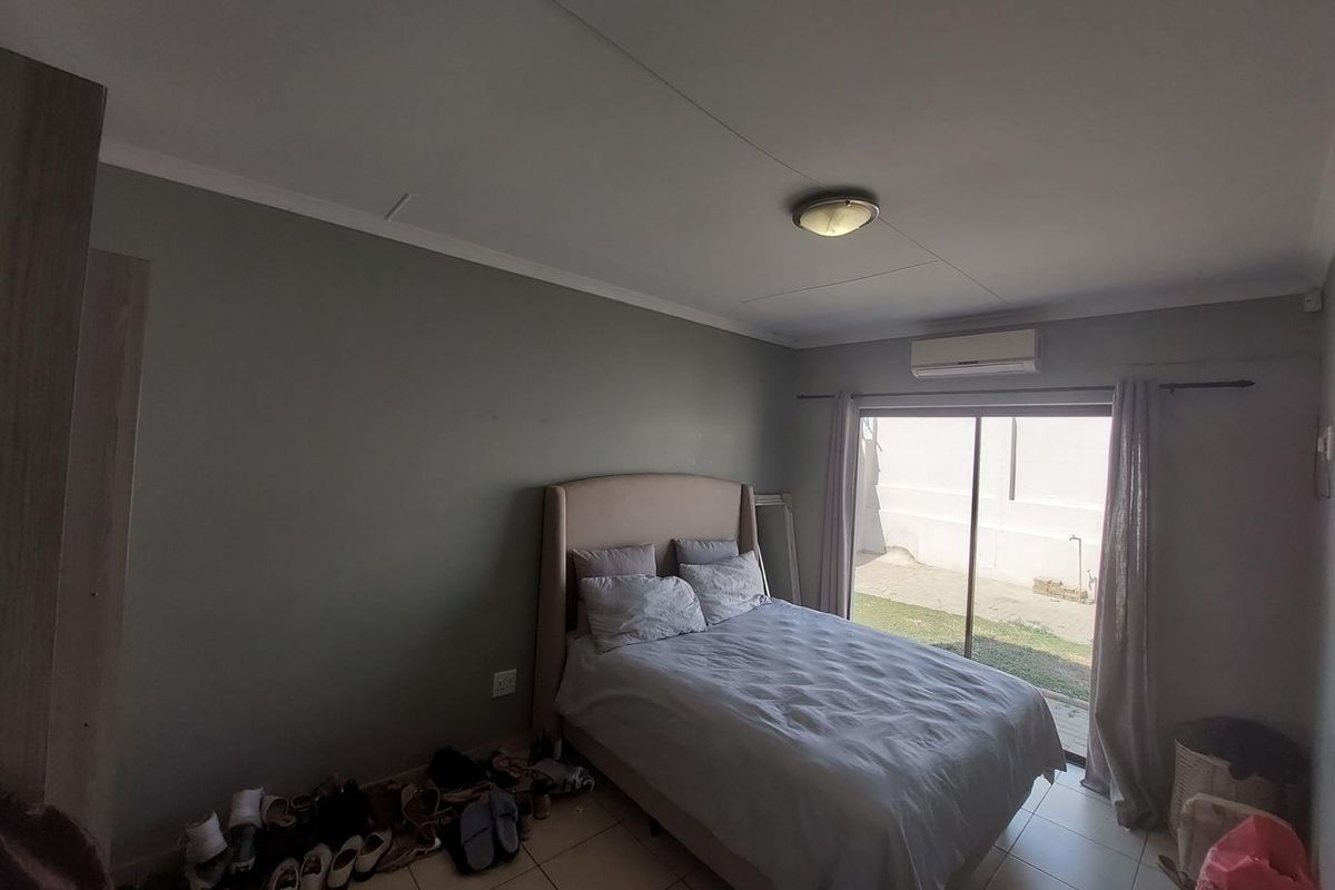A bedroom featuring tiled flooring, a wall-mounted air conditioning unit, and sliding glass doors providing direct access to the rear garden area.