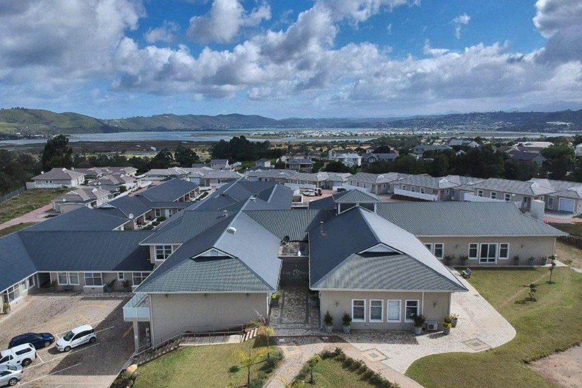 Aerial view of a residential complex featuring metal roofing, paved driveways, and landscaped grounds with scenic coastal and mountain views in the background.