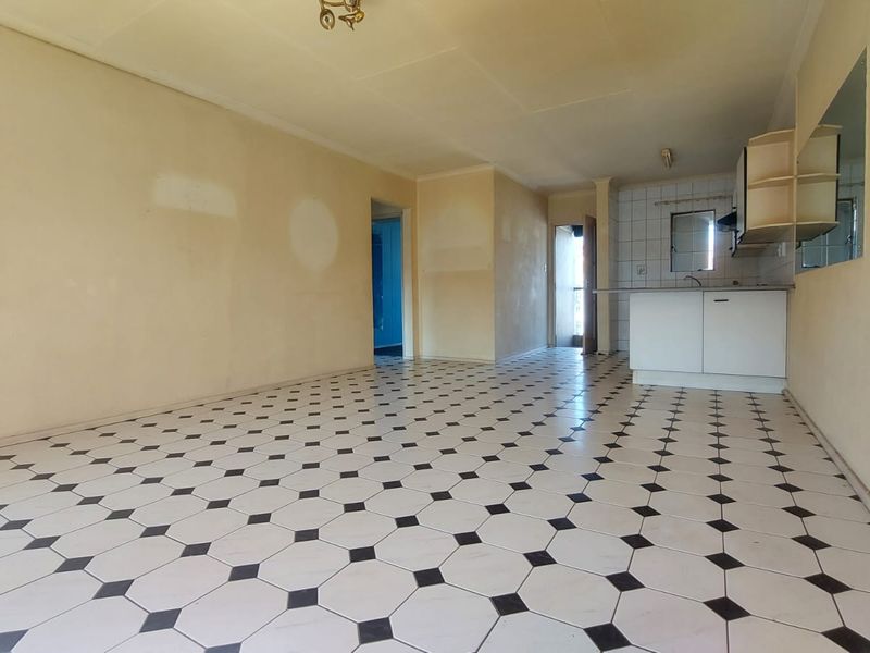 An empty open-plan living and kitchen area featuring tiled flooring and basic cabinetry, offering a blank canvas for renovation and modernization.