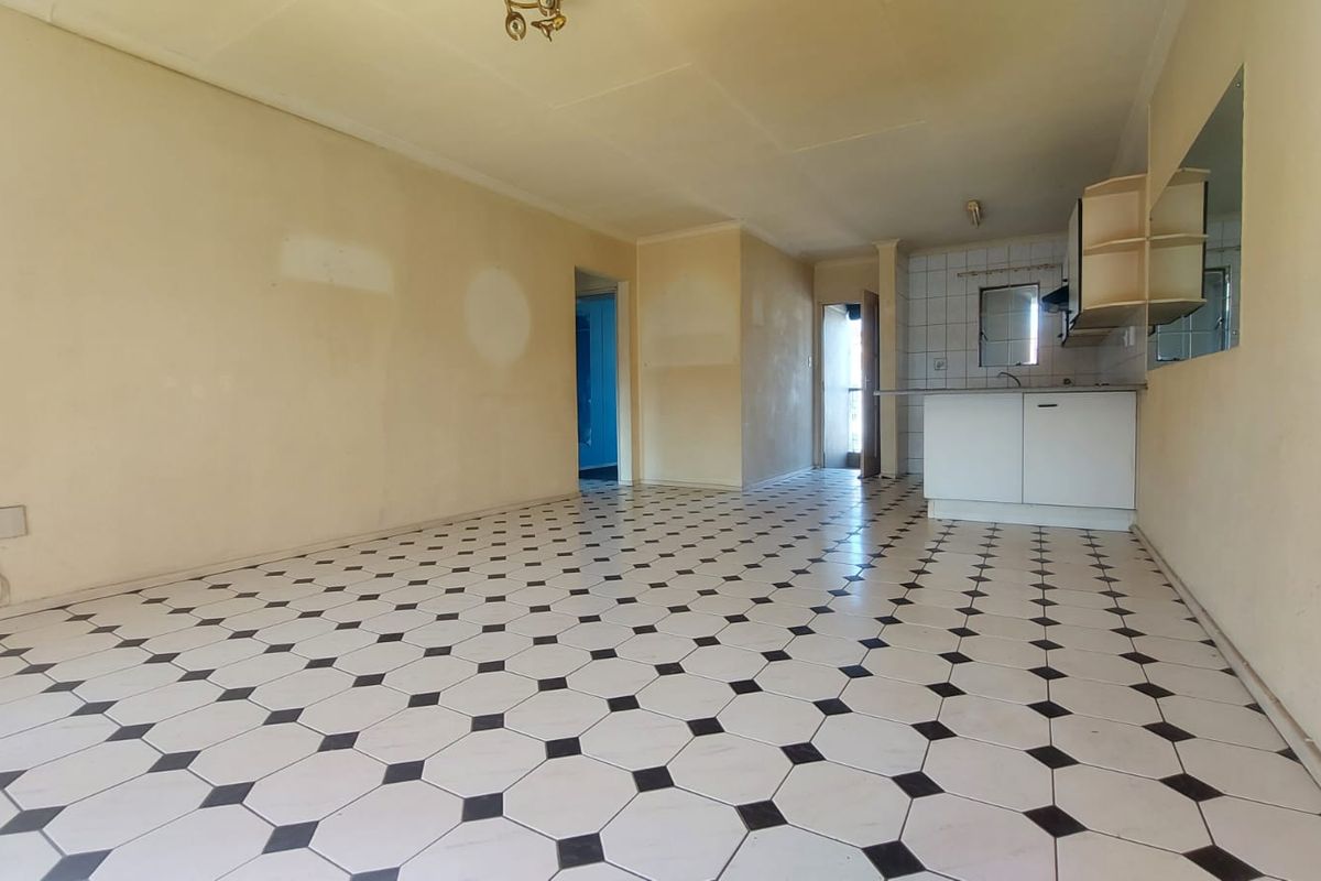 An empty open-plan living and kitchen area featuring tiled flooring and basic cabinetry, offering a blank canvas for renovation and modernization.