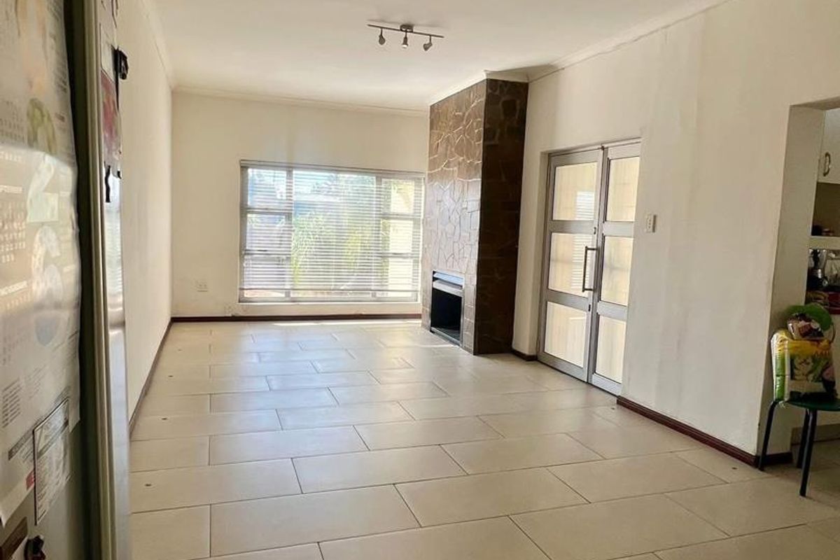 Spacious living area featuring large format floor tiles, a prominent stone-clad fireplace, and direct access to the exterior through a glass door.