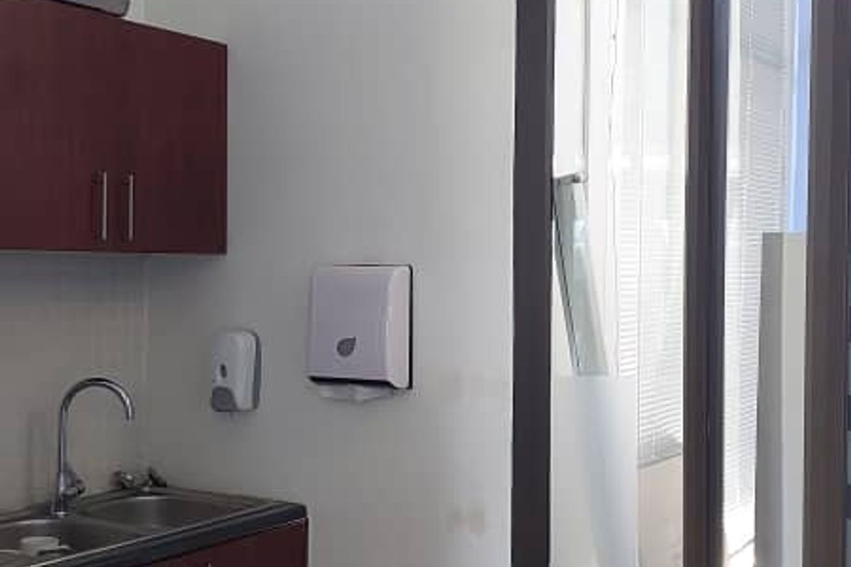 A functional office kitchenette area featuring dark wood cabinetry, a stainless steel sink, and tiled flooring, adjacent to a large glass partition.