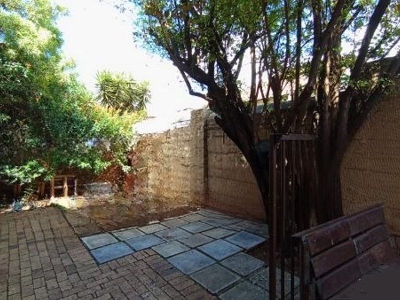 A private rear courtyard featuring a mix of brick and stone paving, enclosed by a boundary wall with established trees.