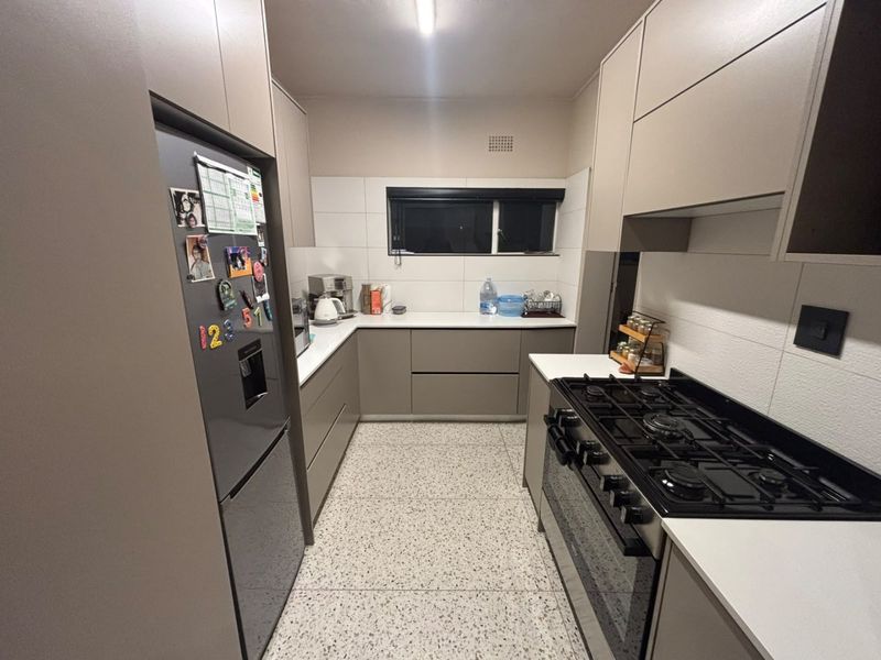 Modern galley-style kitchen featuring sleek handleless cabinetry, stone countertops, a gas stove with oven, and durable terrazzo flooring.