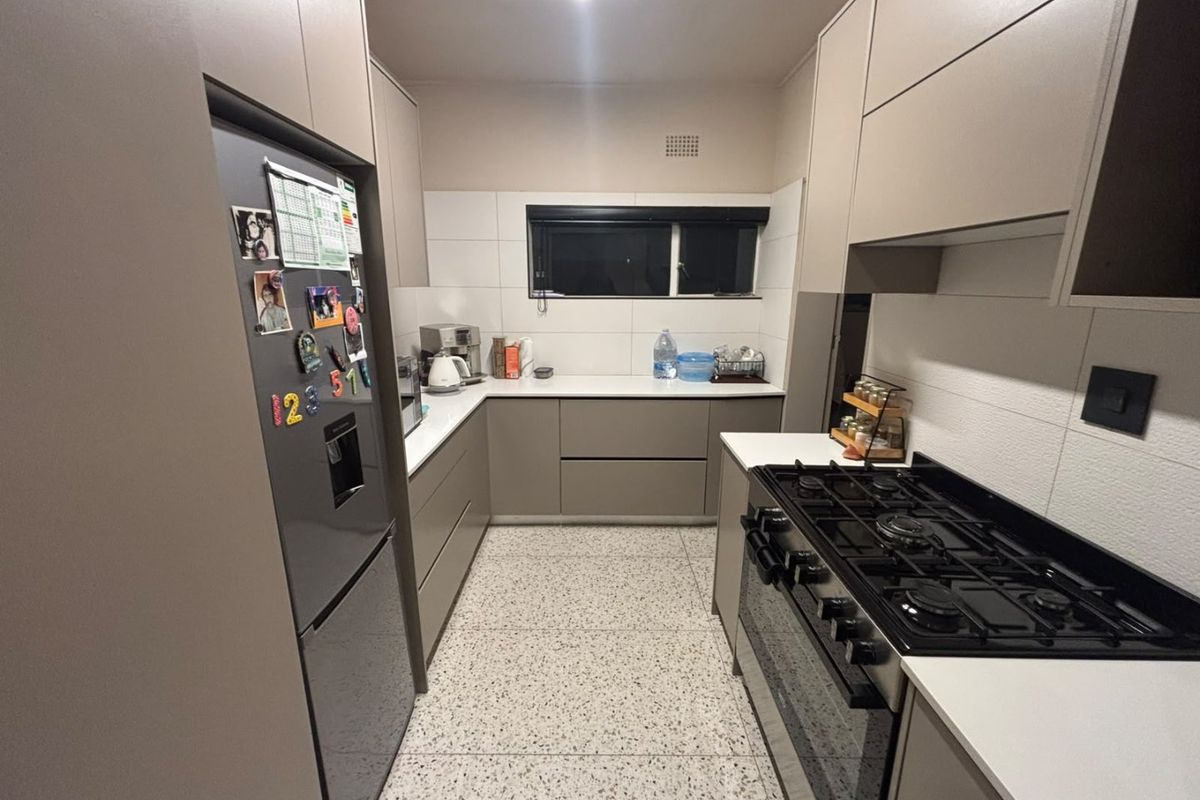 Modern galley-style kitchen featuring sleek handleless cabinetry, stone countertops, a gas stove with oven, and durable terrazzo flooring.