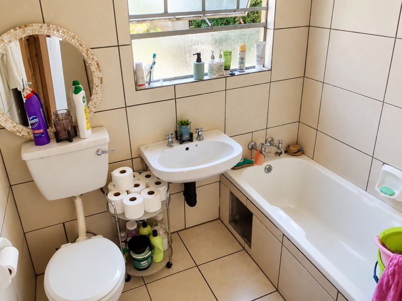 A compact bathroom featuring a standard bathtub, wall-mounted basin, and toilet with neutral wall and floor tiling throughout.