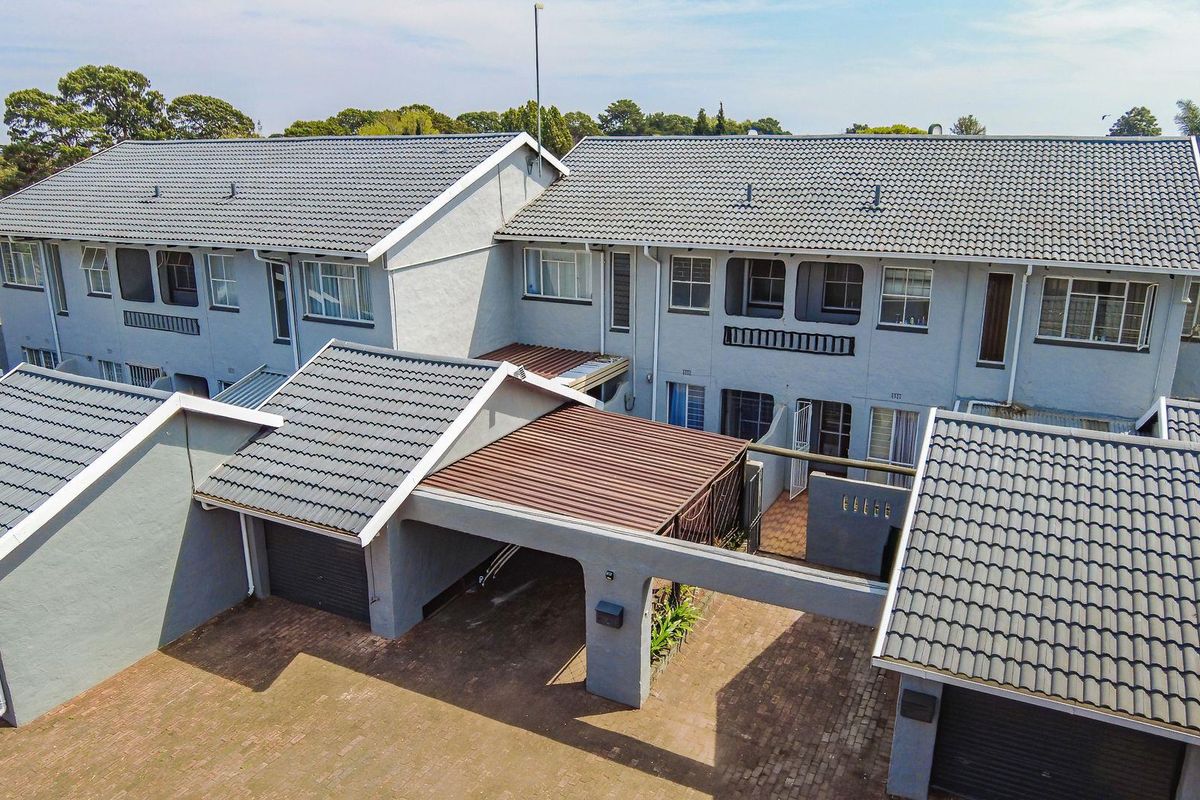 Aerial view of a townhouse complex featuring tiled roofs, paved driveways, garages, and covered carports with balconies on the upper level.