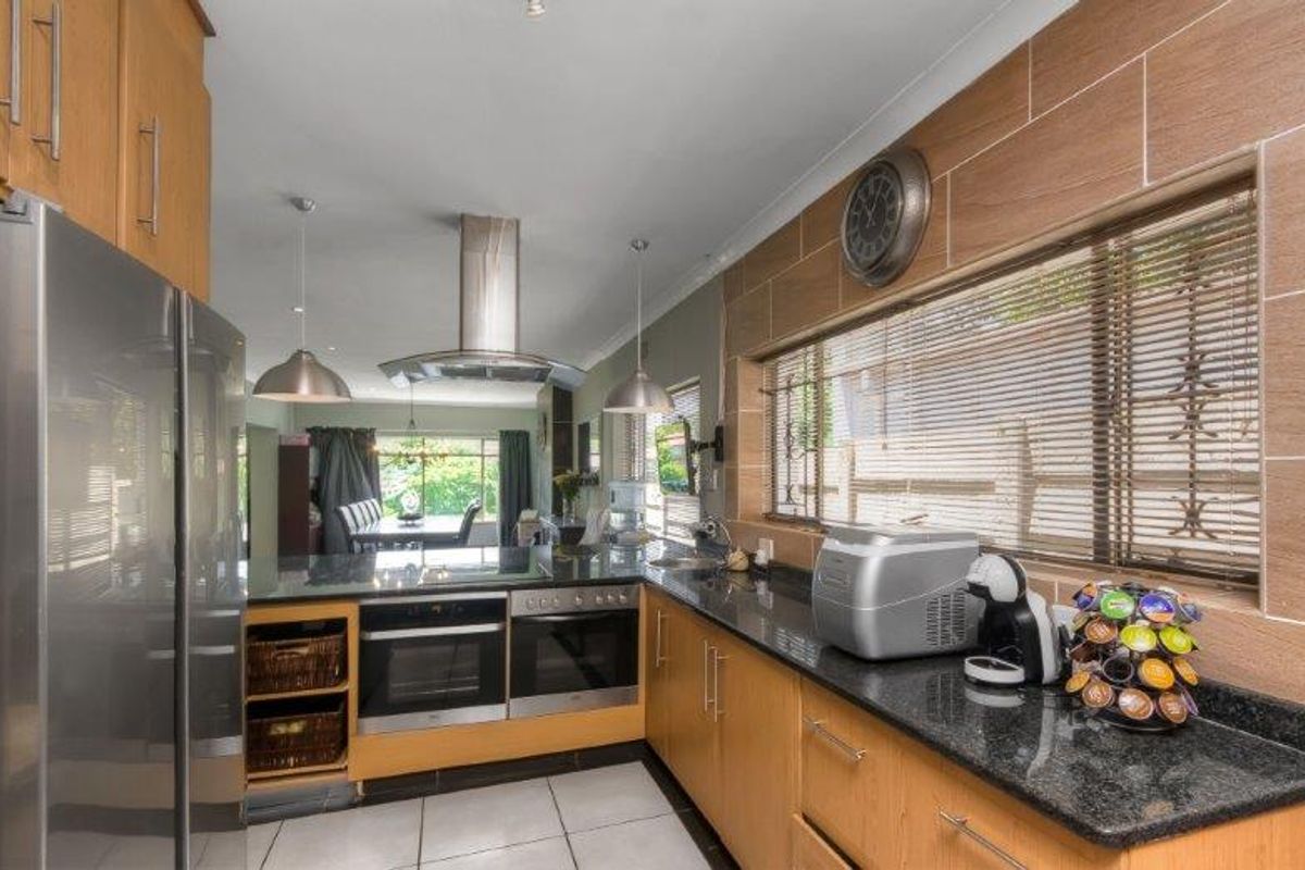 A functional kitchen featuring light wood cabinetry, granite countertops, built-in ovens, and a modern extractor fan, with an open-plan flow to the dining area.