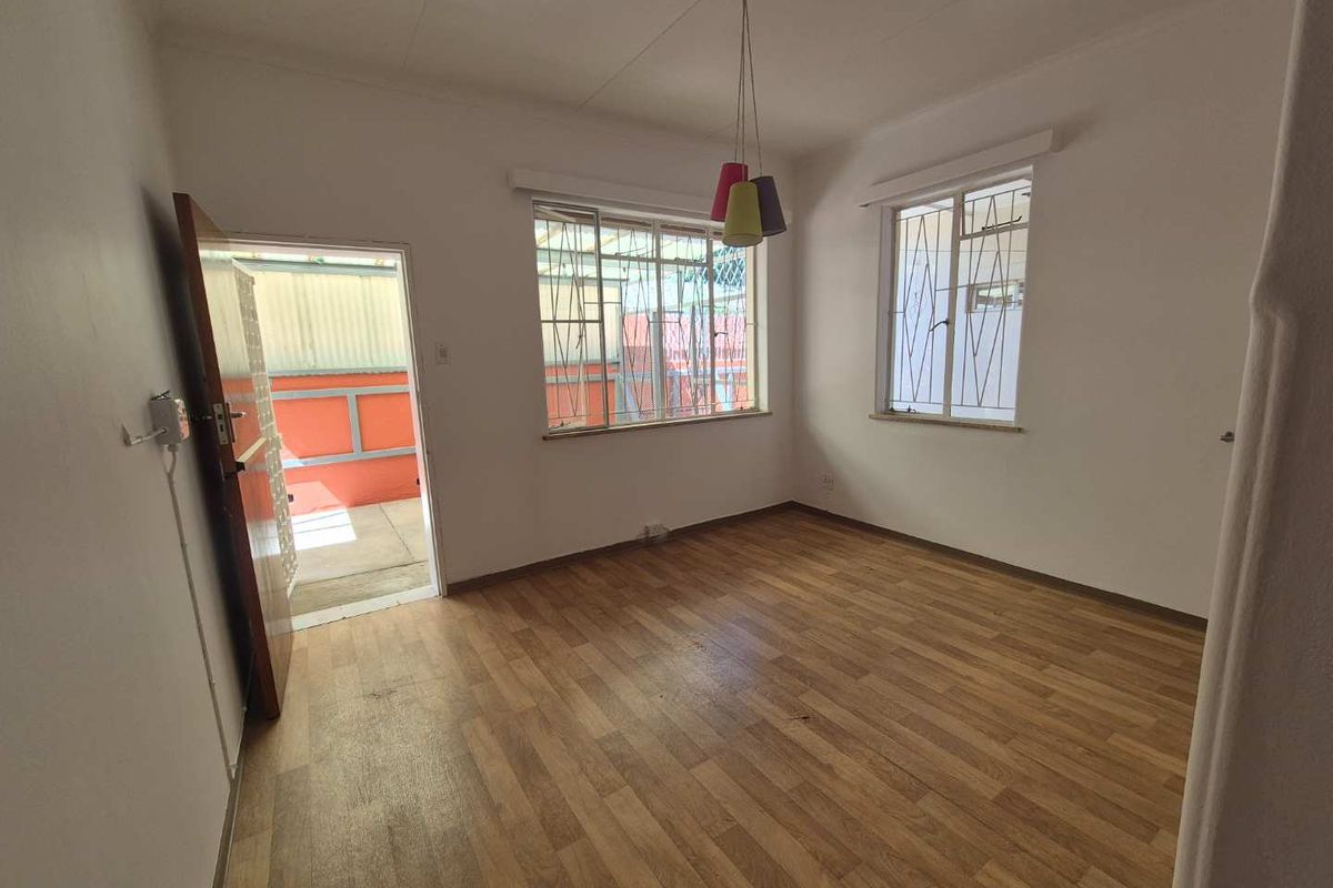 A bright, empty living room featuring wood-look flooring, security bars on windows, and direct access to an outdoor area.