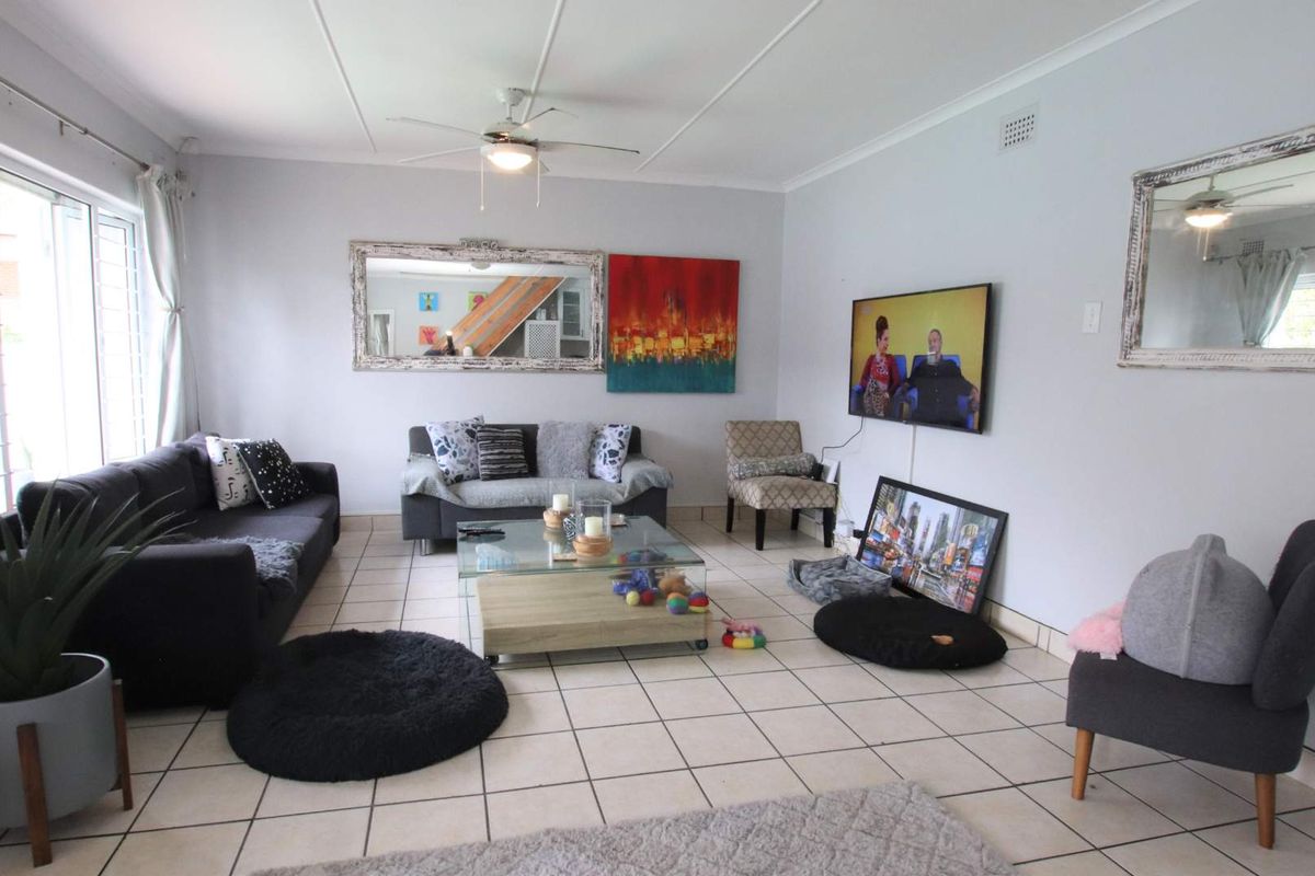 A spacious living room featuring tiled flooring, a ceiling fan, and large windows allowing for natural light.
